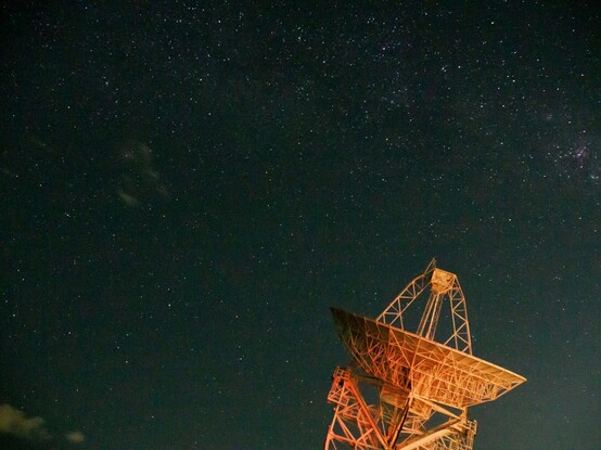 The night sky in the middle of the night with a radio telescope visible.