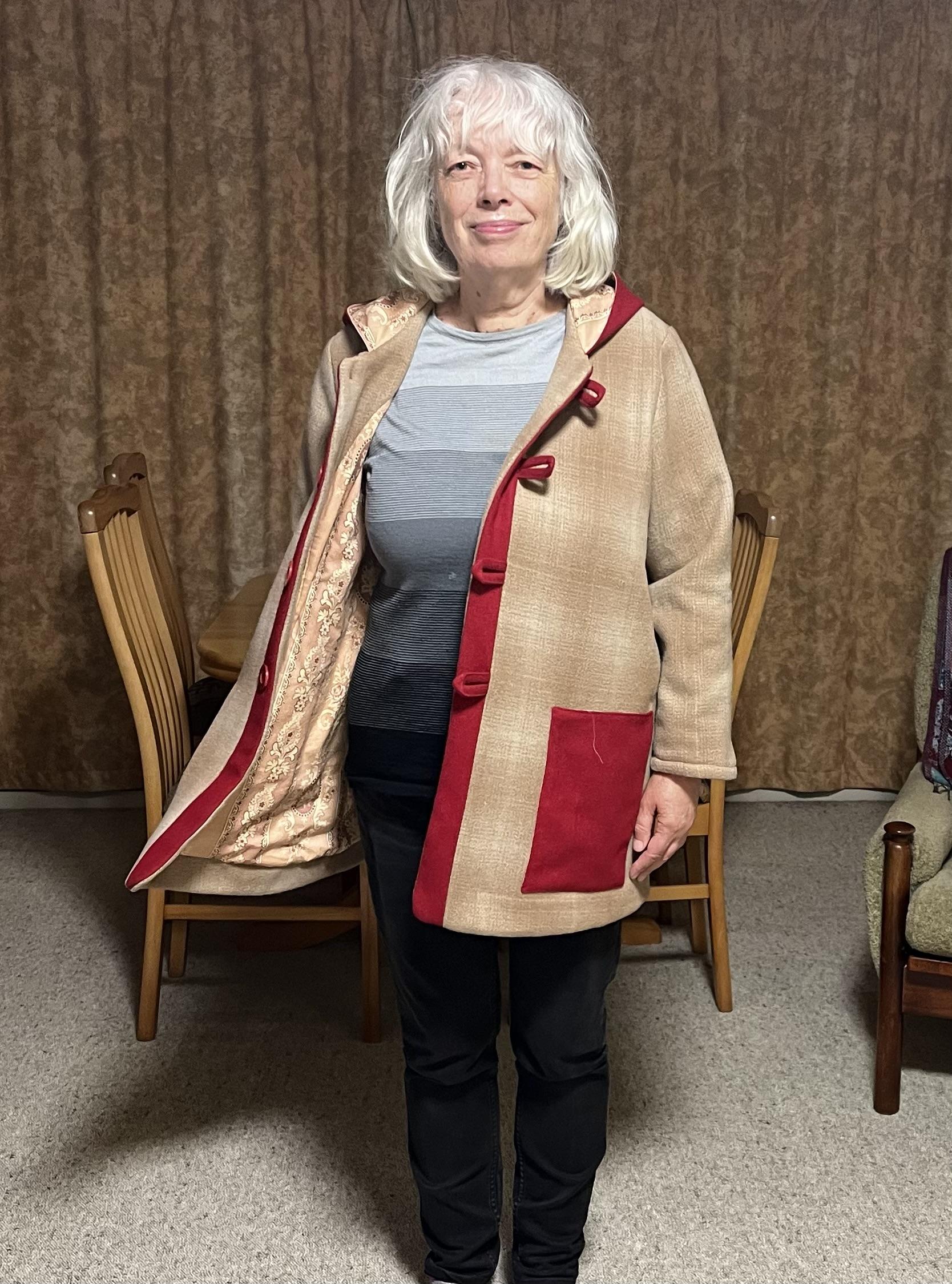 Me wearing the same coat with the hood down and front open to show off the lining. Under the coat I’m wearing a grey striped top and skinny grey jeans.