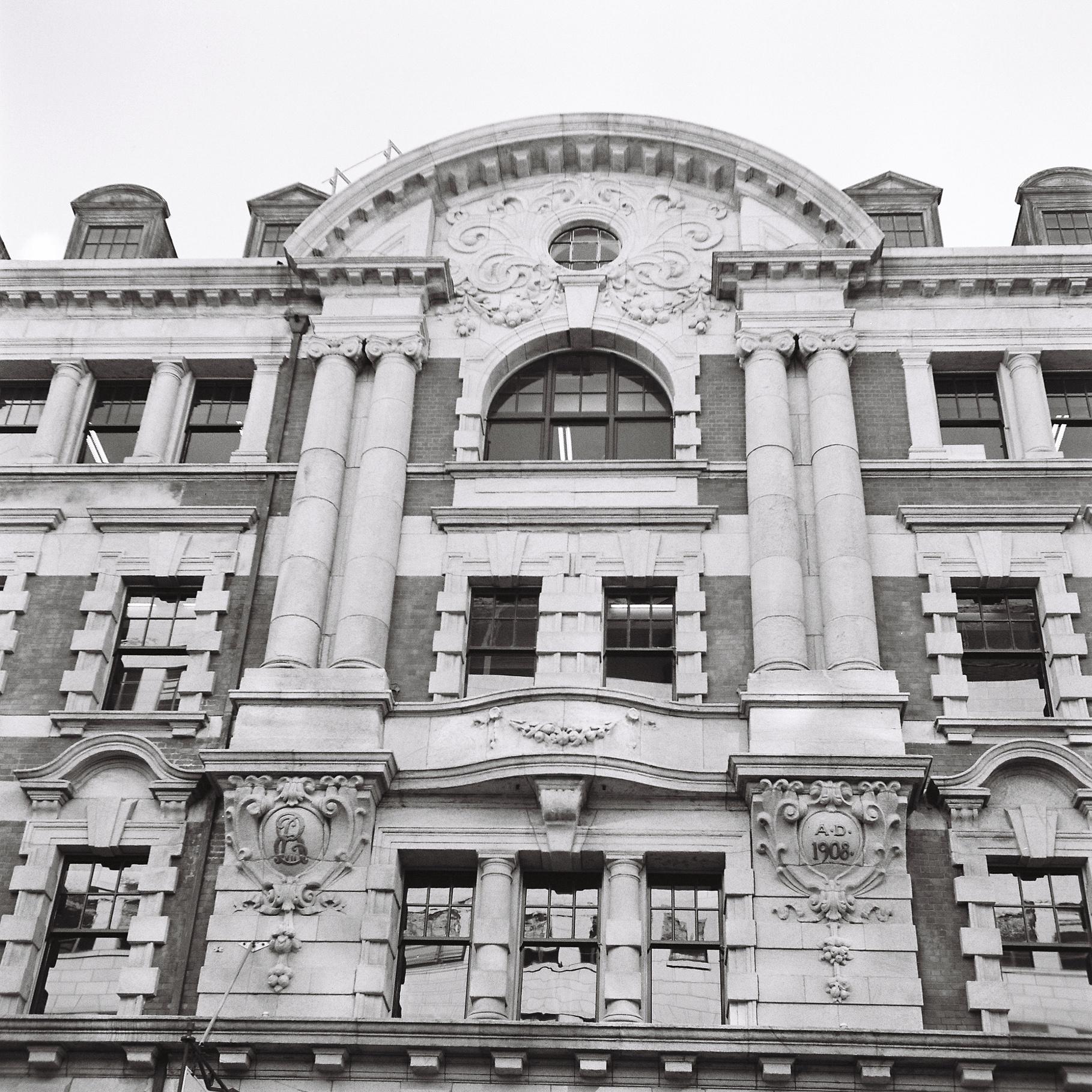 Square black & white photo of a 4-5 story Wellington office building in classic style with white stone pillars and brick walls.
Photo was shot on a Yashica B twin-lens reflex camera & Kodak 400TX film